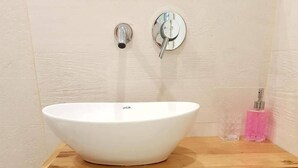 A modern bathroom with a white vessel sink, wooden vanity, and a small trash bin. - Royal Apartment Tel Aviv (Tel Aviv)