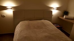 A bedroom with a large bed, headboard, bedside lamps, and a small shelf with a towel and a plant. - Royal Apartment Tel Aviv (Tel Aviv)