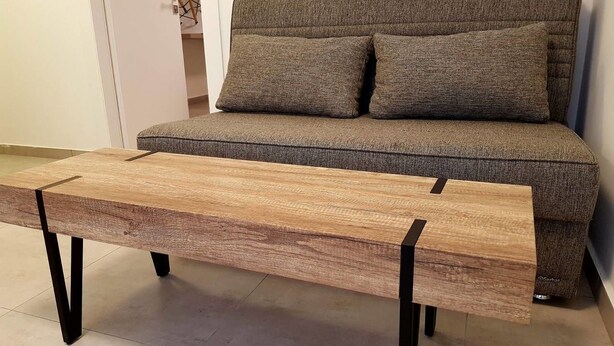 A wooden bench with black metal legs in a room with a grey sofa and a white door. - Royal Apartment Tel Aviv (Tel Aviv)