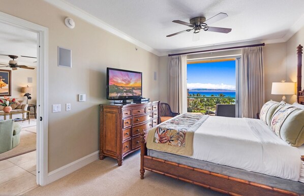 A hotel room with a bed, a television, a dresser, and a view of the ocean.