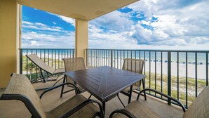 A balcony with a table and chairs, overlooking a beach with a railing.