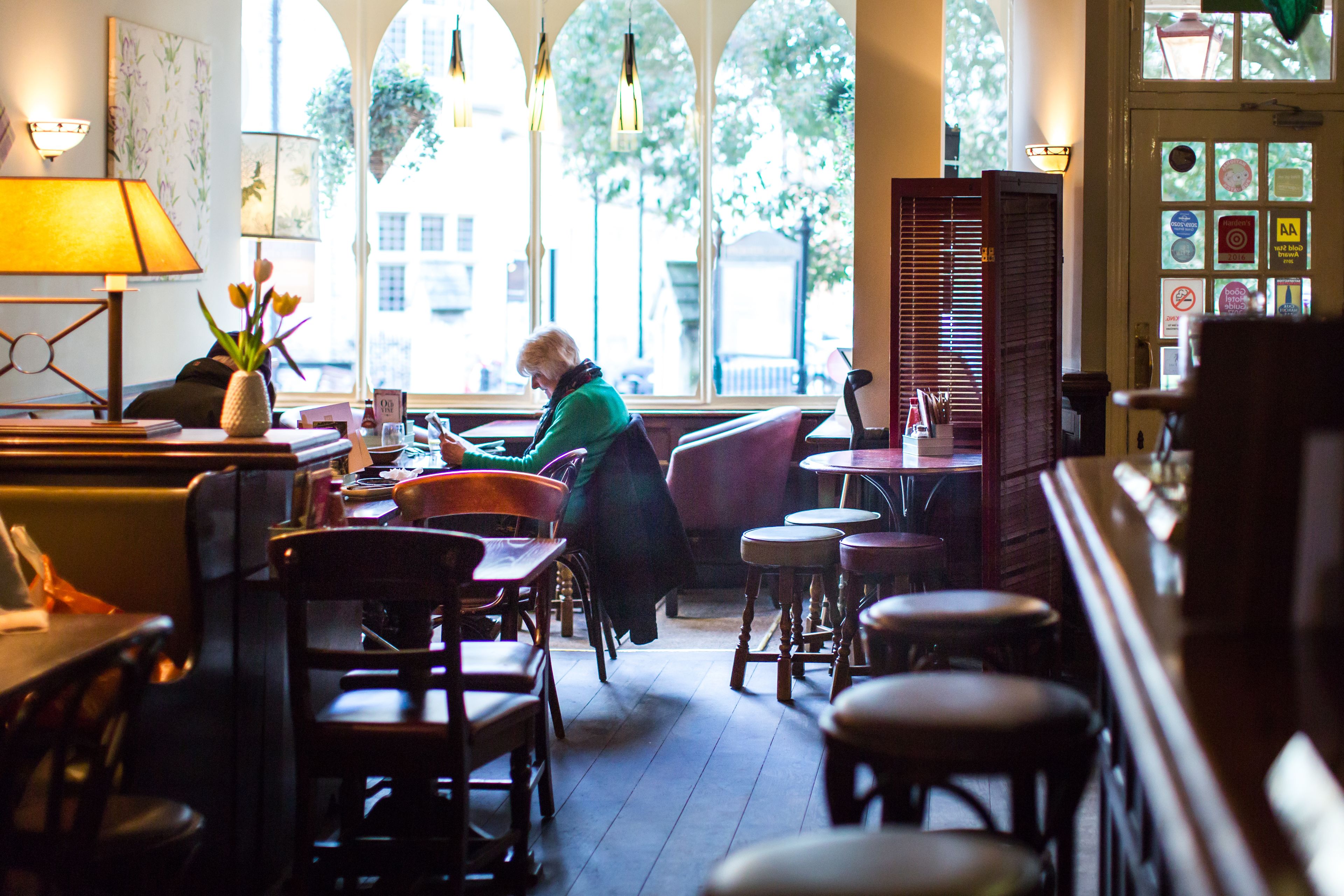 En hyggelig café med træmøbler, et stort vindue med udsigt til træer, og en lampe på bordet.