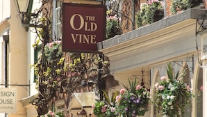 An outdoor seating area of The Old Vine with a signboard, potted plants, and a brick building facade. - The Old Vine (Winchester)