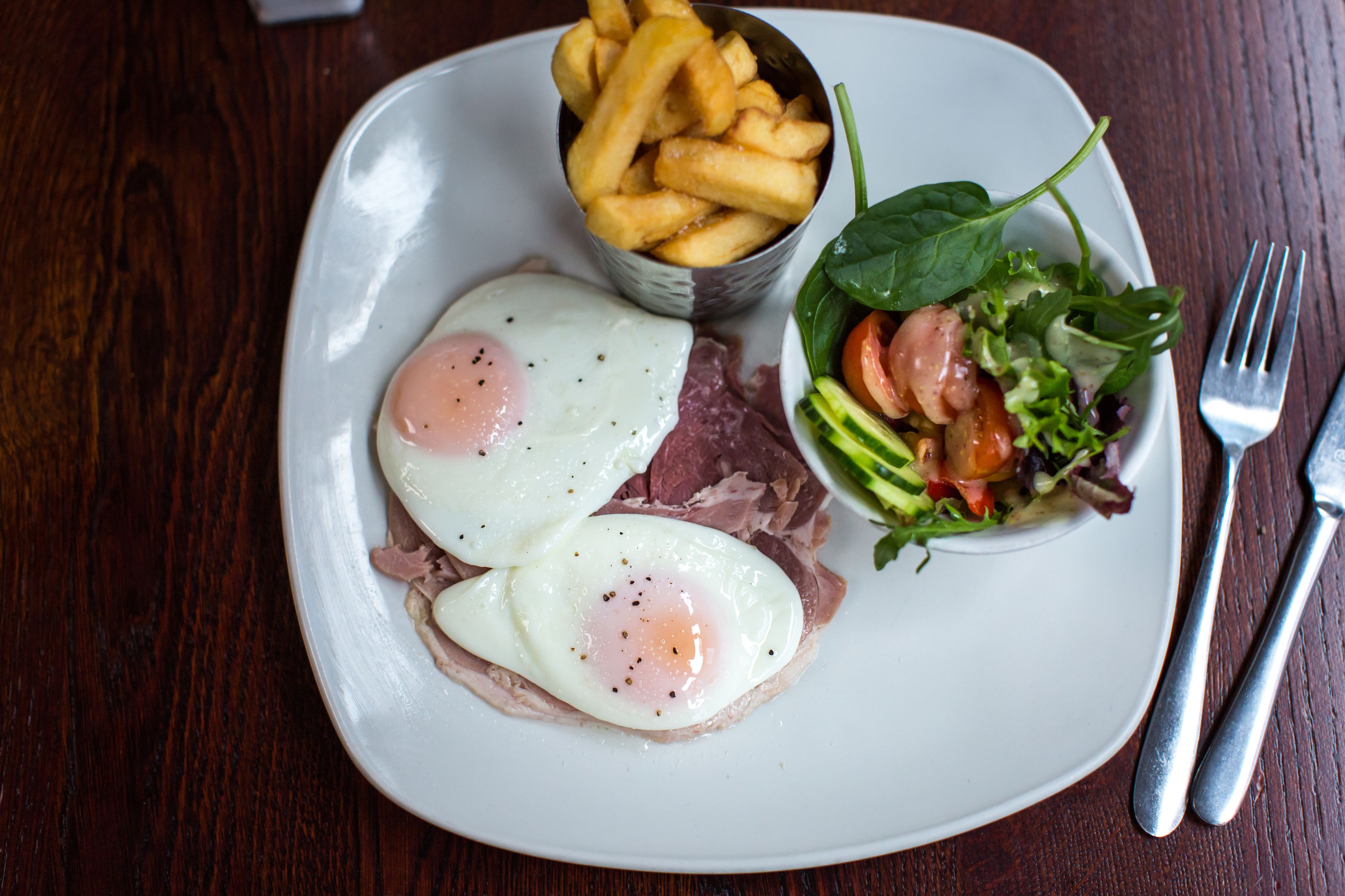 A plate with eggs, meat, fries, and a salad.