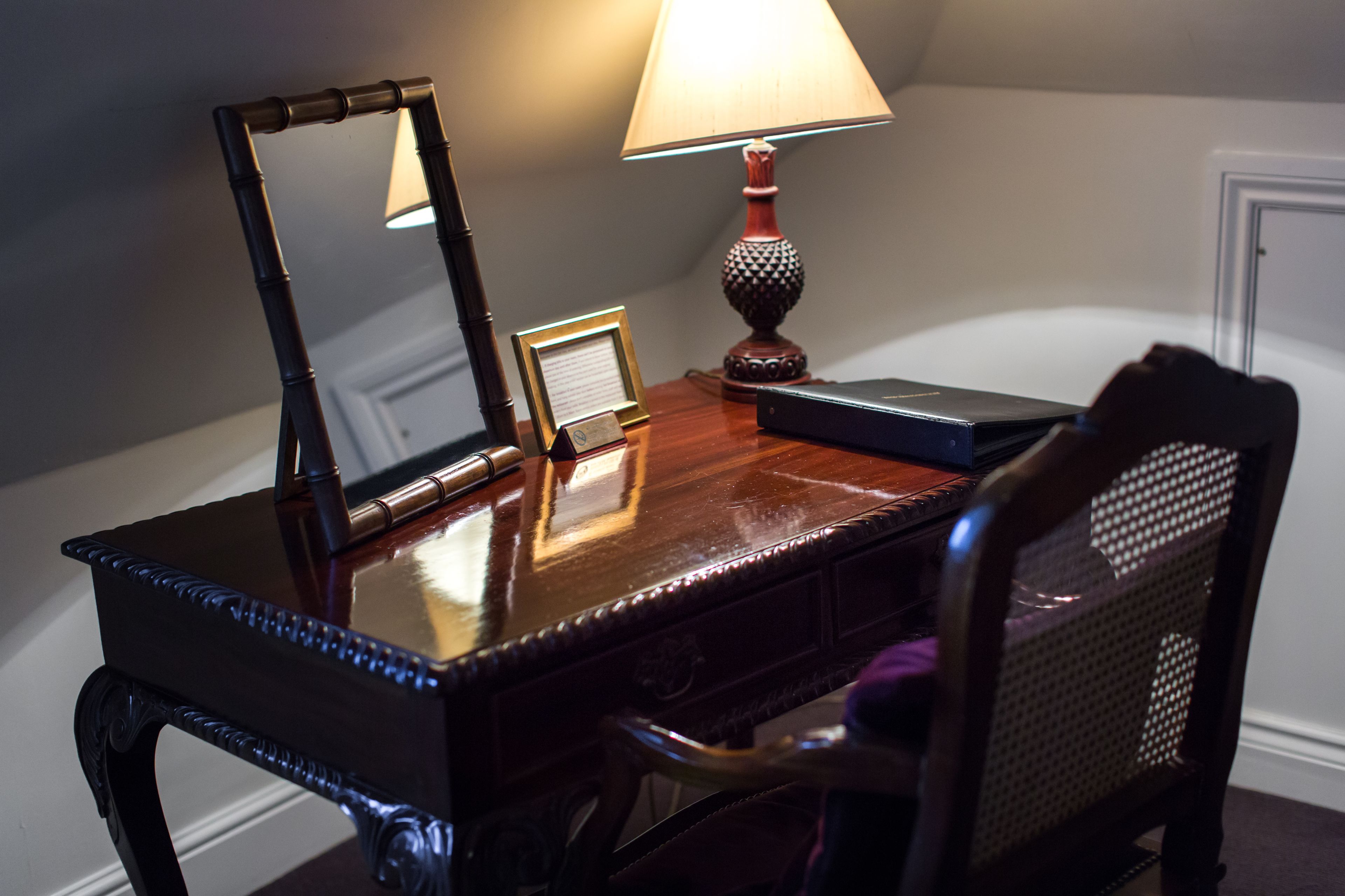 A wooden desk with a mirror, a lamp, and a framed picture.