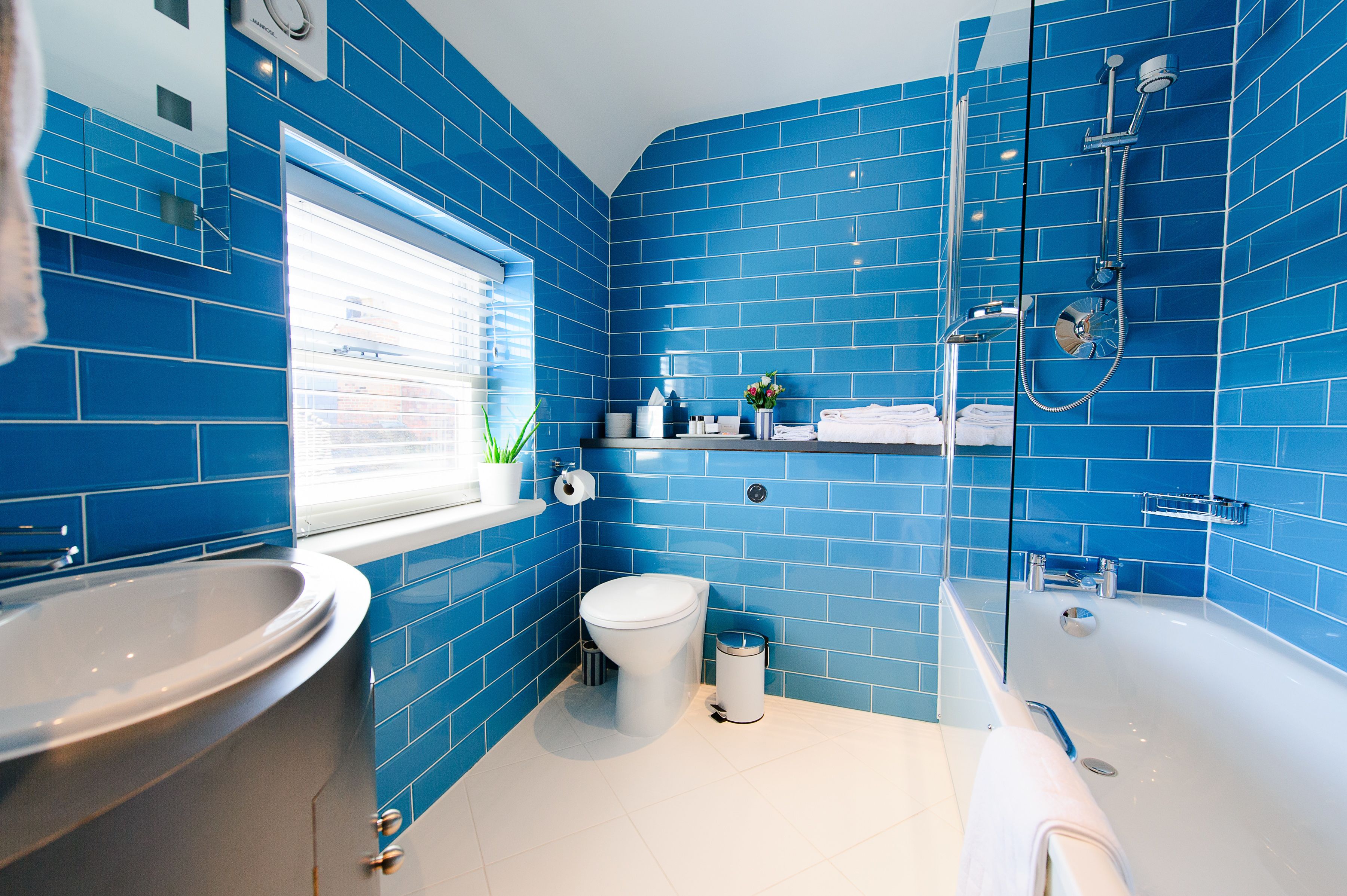 A bathroom with blue tiles, a white toilet, a sink, and a bathtub.