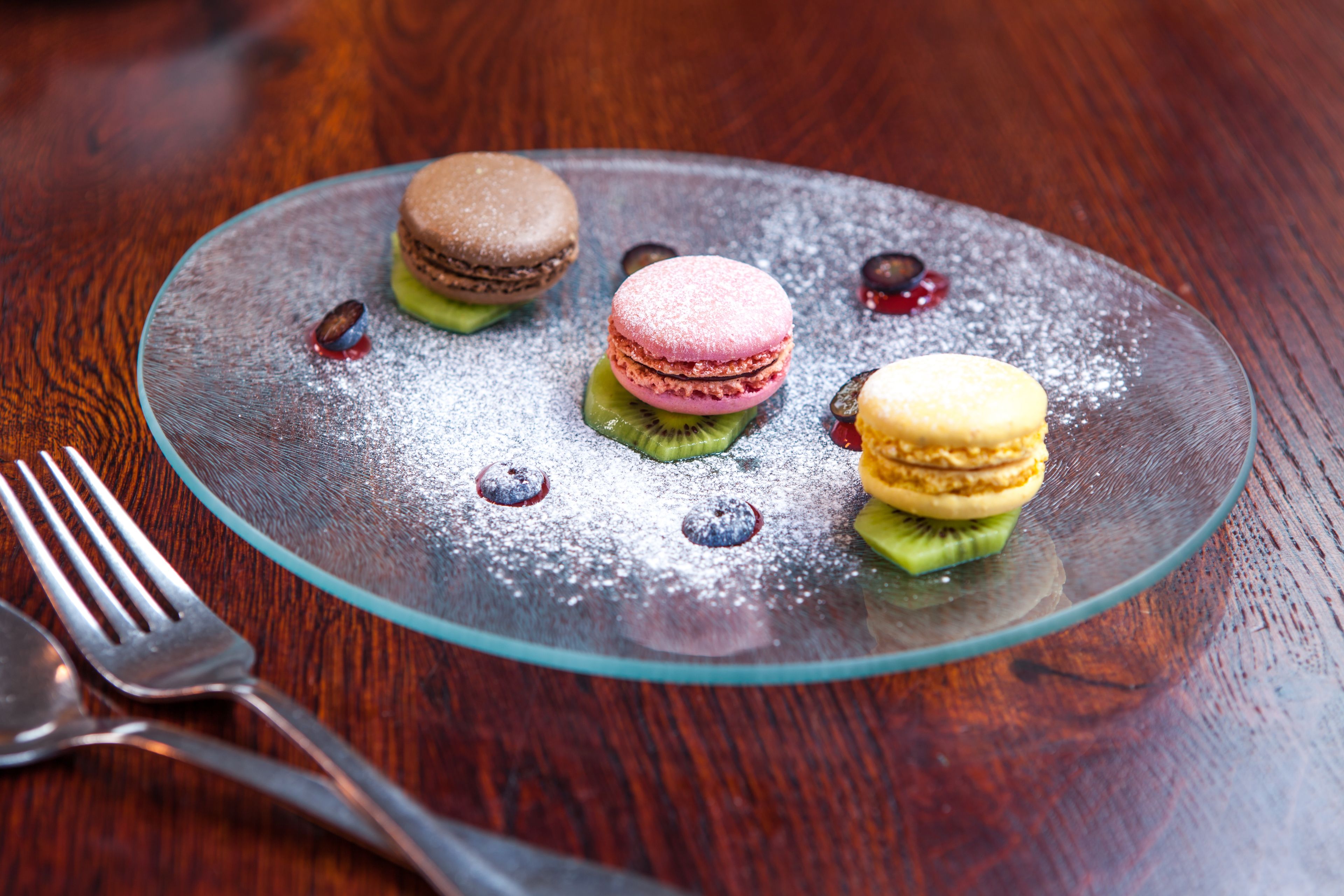 A dessert plate with three macarons and a spoon on a wooden table.