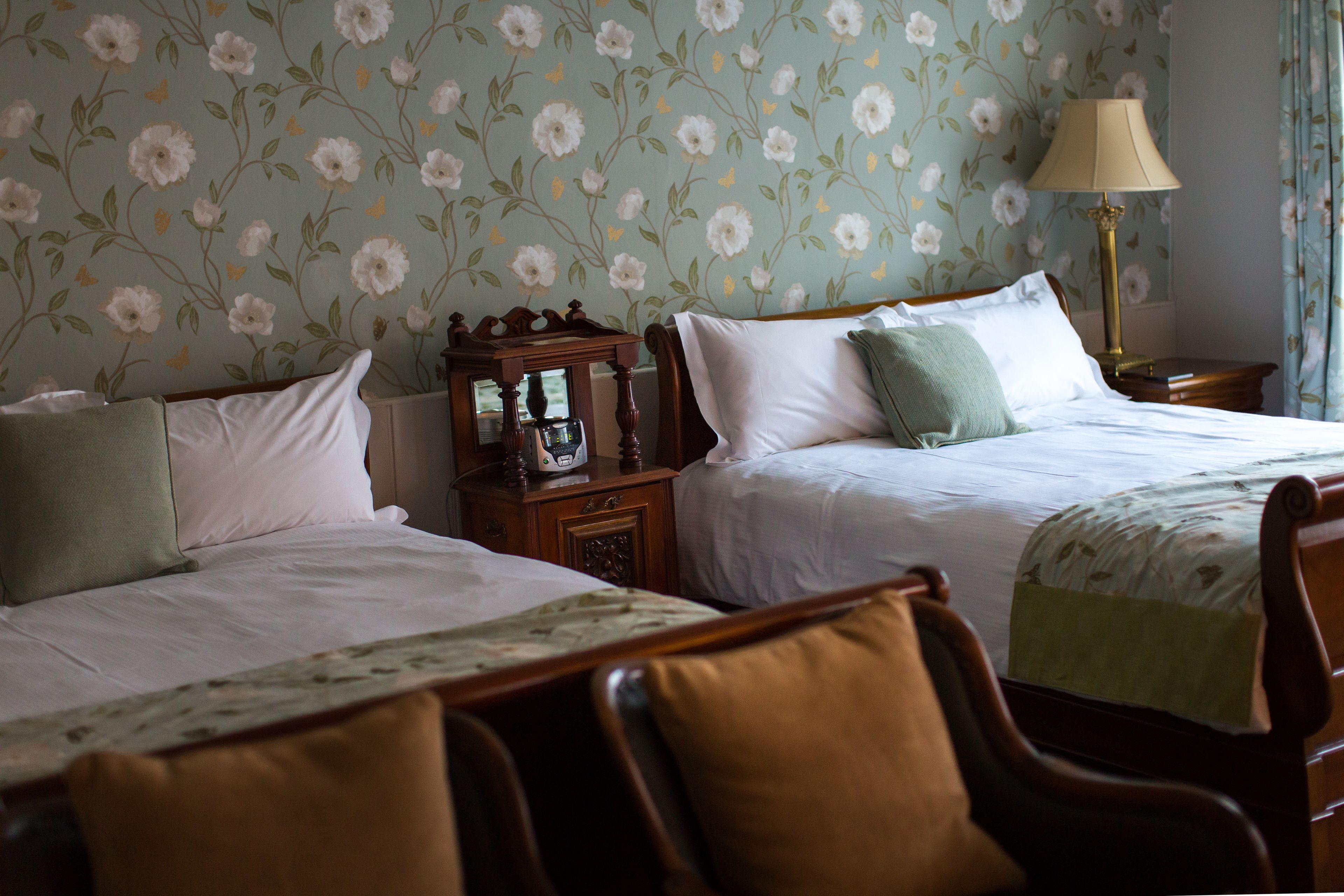 Ein Hotelzimmer mit zwei Betten, einem Nachttisch mit Lampe und blumengemusterten Tapeten.