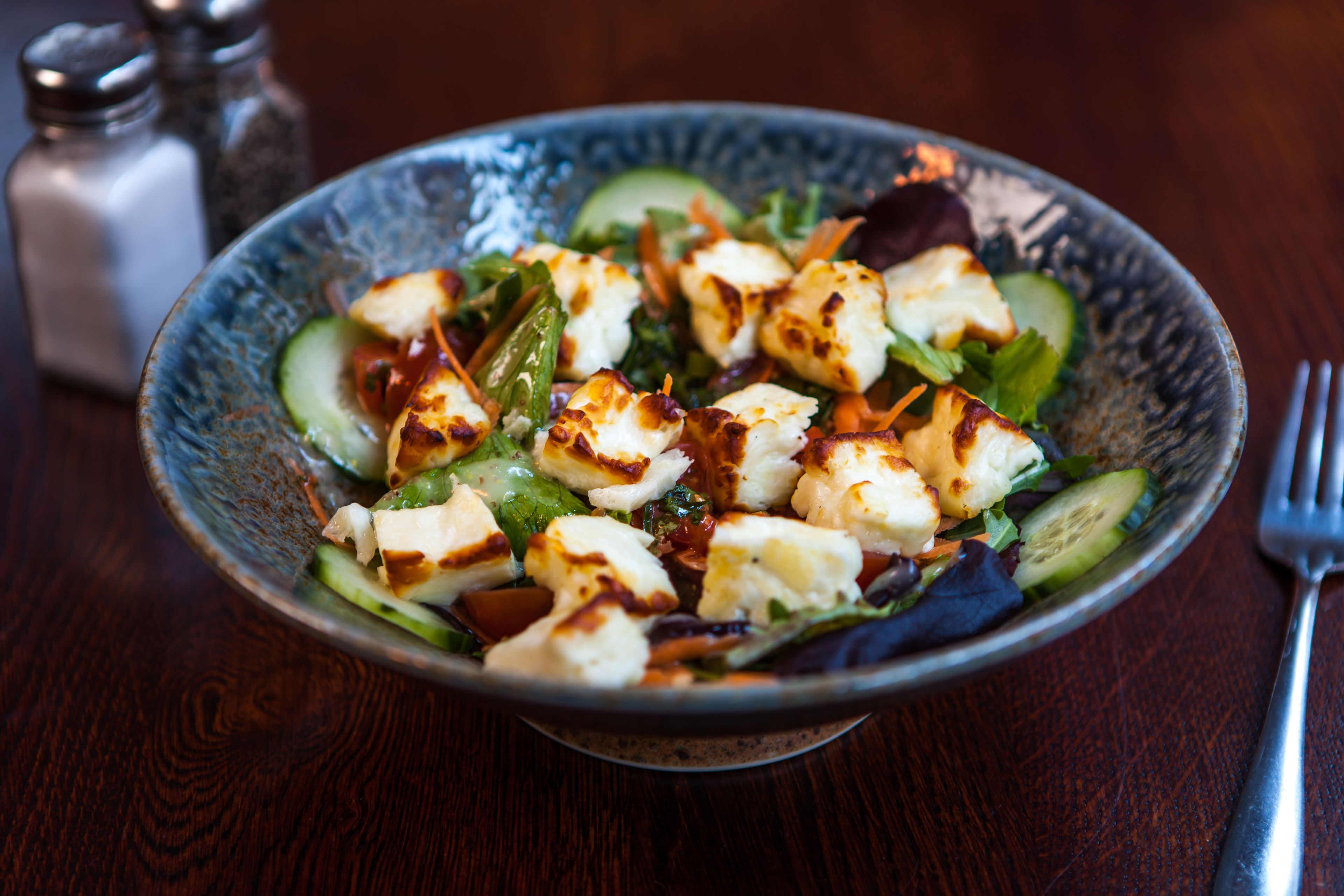 A bowl of salad with grilled chicken and vegetables on a wooden table.
