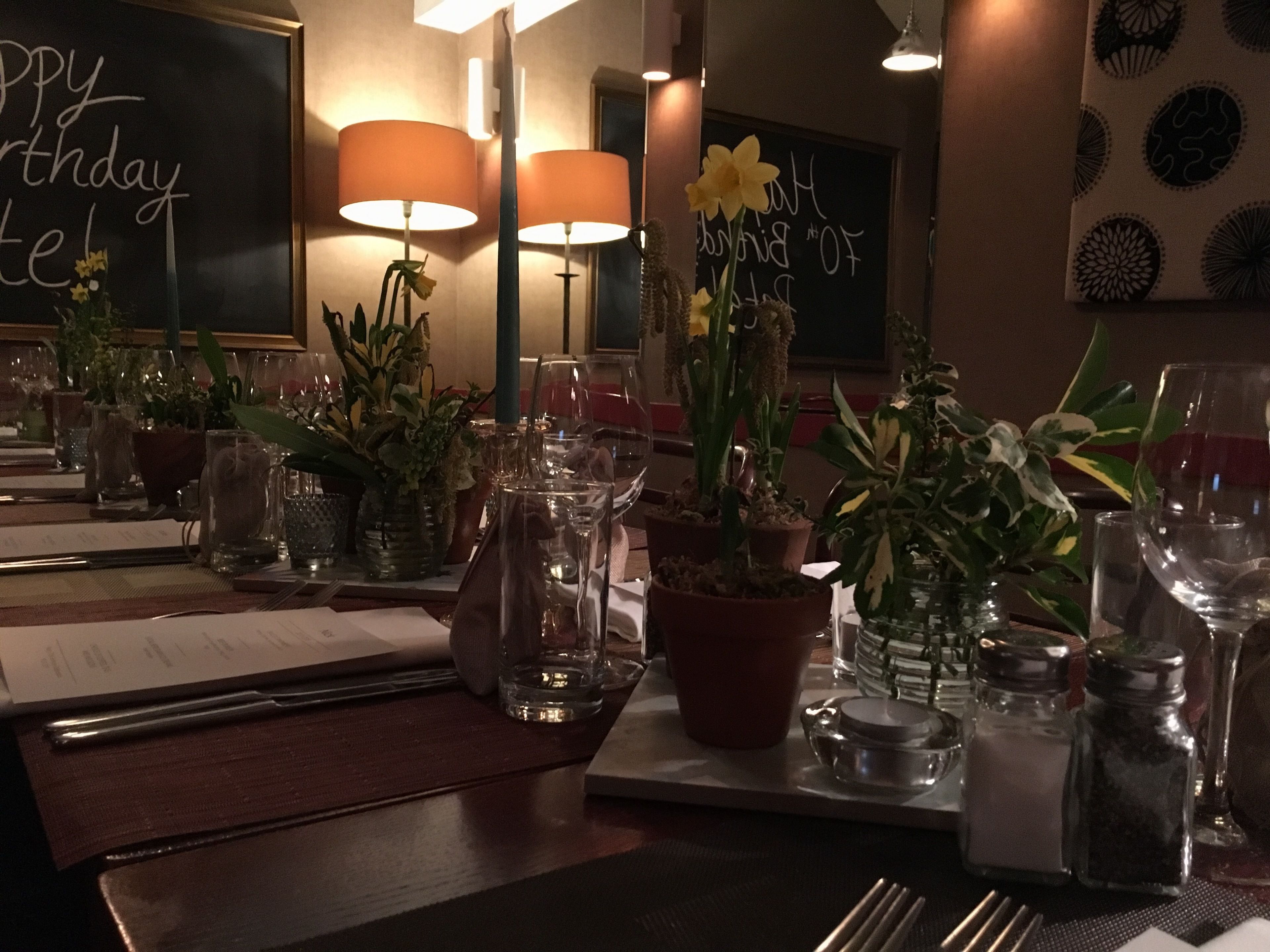 Ett restaurangbord dukat med vinglas, tallrikar, bestick och krukväxter.