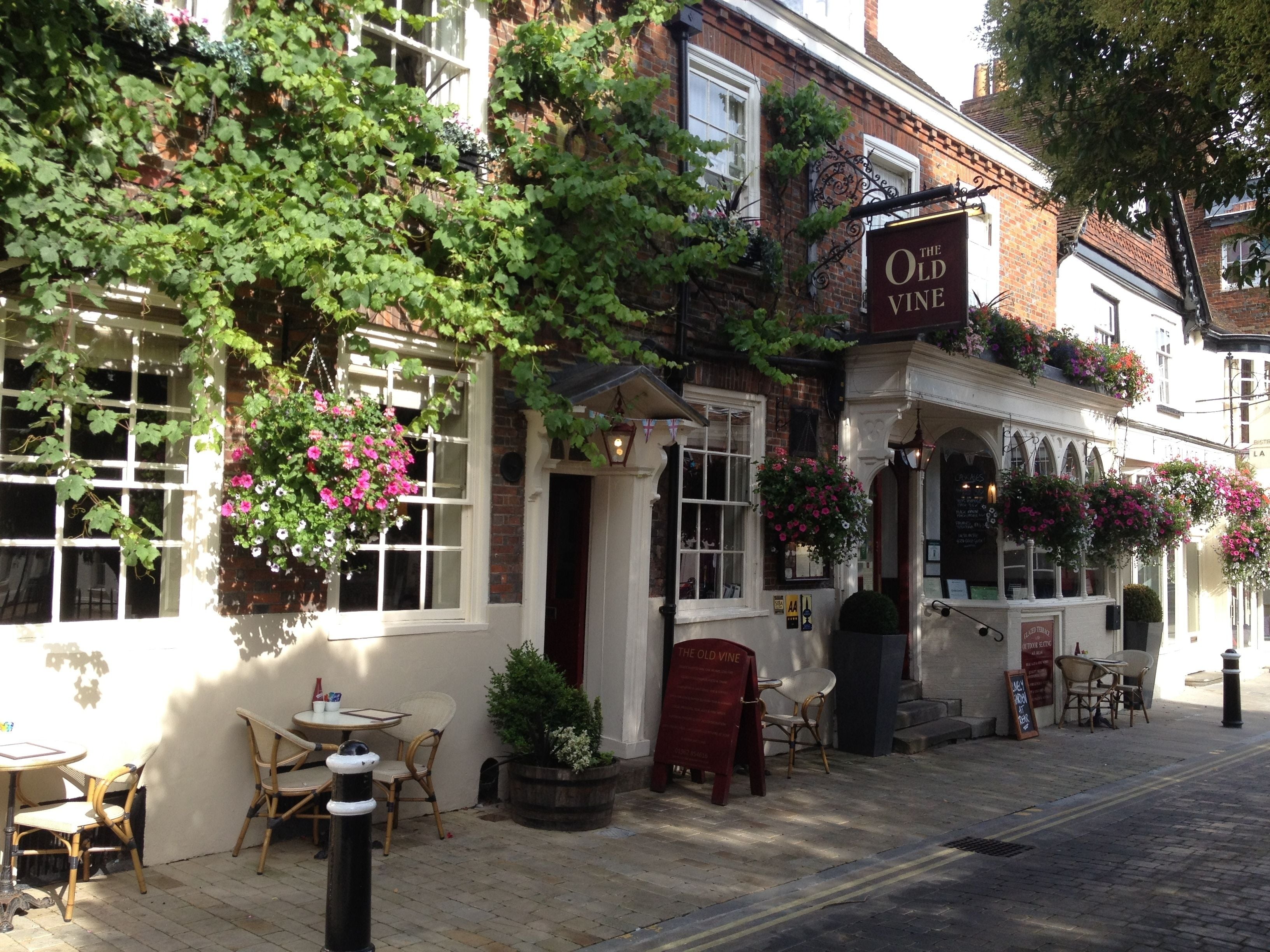 A traditional pub with outdoor seating, a sign reading "The Old Vine," and hanging flower baskets.