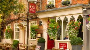 A traditional brick building with a red door, multiple windows, and outdoor seating area with wicker chairs. - The Old Vine (Winchester)