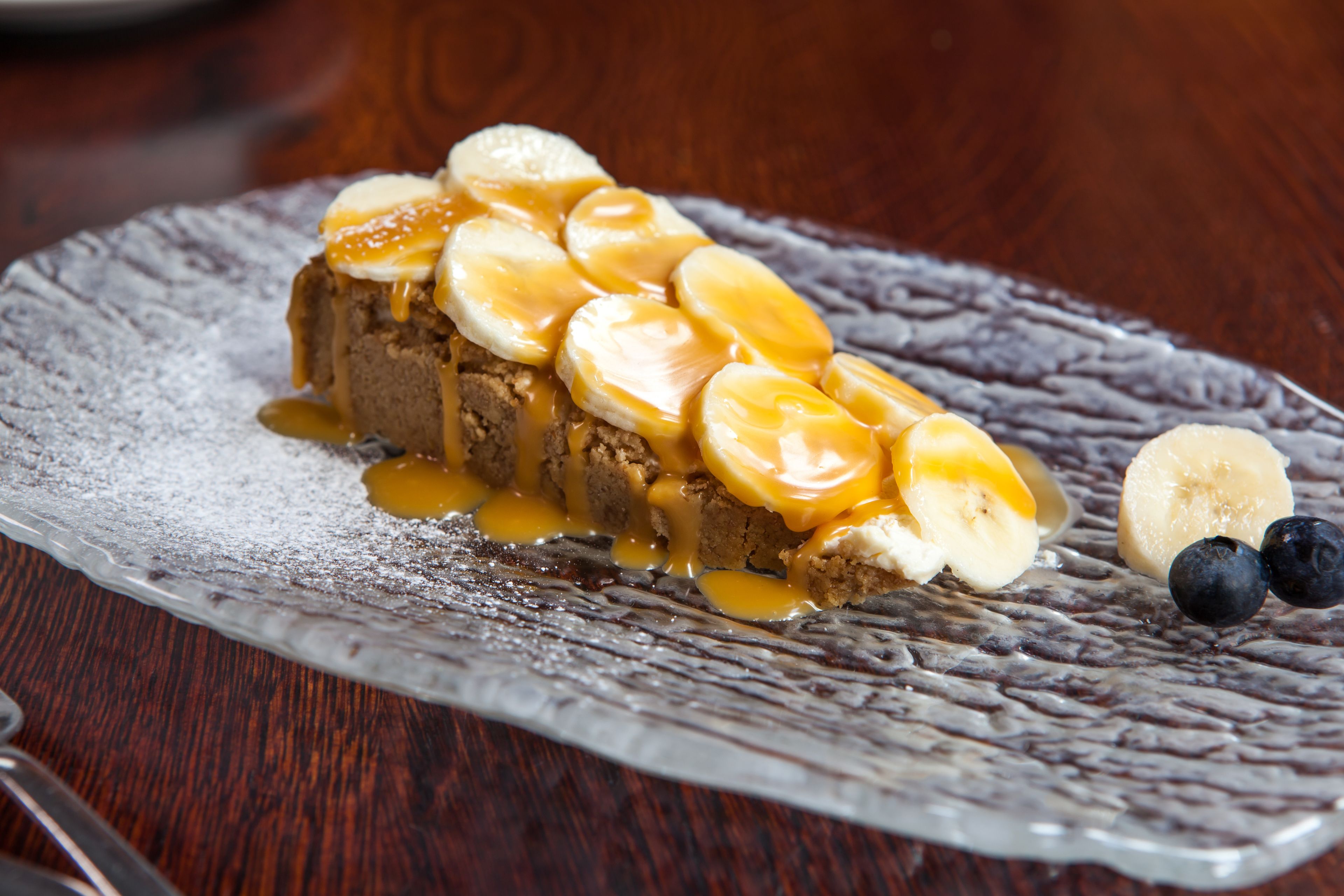 Un postre sobre un plato con textura, acompañado de plátanos y salsa de caramelo.