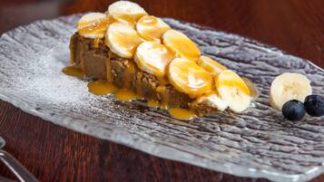 Un postre sobre un plato con textura, acompañado de plátanos y salsa de caramelo.