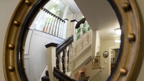 A round mirror with a gold frame reflecting a staircase with white balusters and dark steps. - The Old Vine (Winchester)