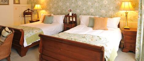 A hotel room with two wooden beds, a wooden chair, two nightstands with lamps, and floral wallpaper.