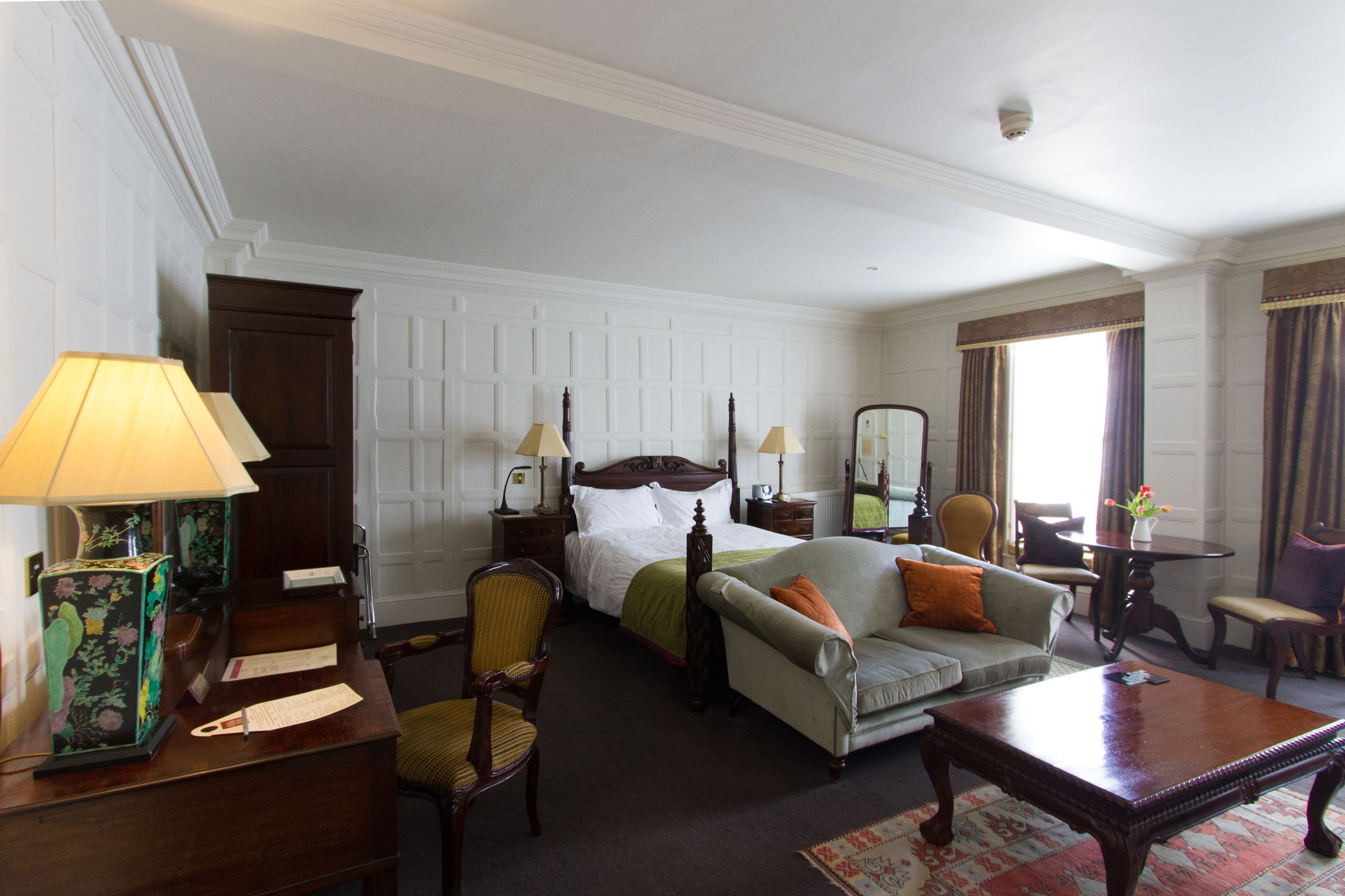 A hotel room with a bed, a sofa, a chair, a table, and a lamp.