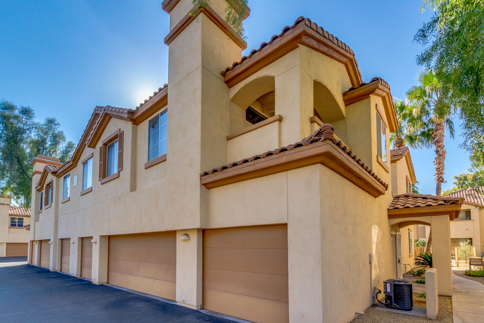 A two-story building with a beige facade, multiple garage doors, and a small balcony.