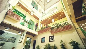 Ein mehrgeschossiges Atrium mit Back- und weißen Wänden, grünen Geländern und mehreren Sitzebenen.