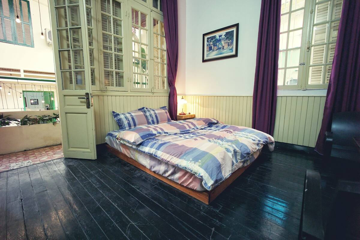 A bedroom with a bed, a nightstand, a window with curtains, and a picture on the wall.
