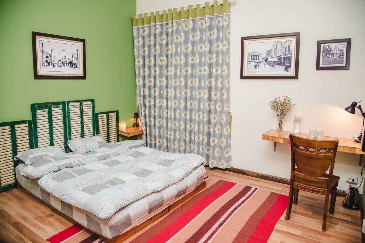 A bedroom with a bed, a chair, a desk, and a window with curtains.