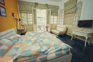 Un dormitorio con cama, una silla, una mesita, televisión y ventana con cortinas.