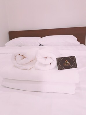 A neatly made bed with white linens and a folded towel, a black card with the text "AIRSTAR" on it, and a wooden headboard.