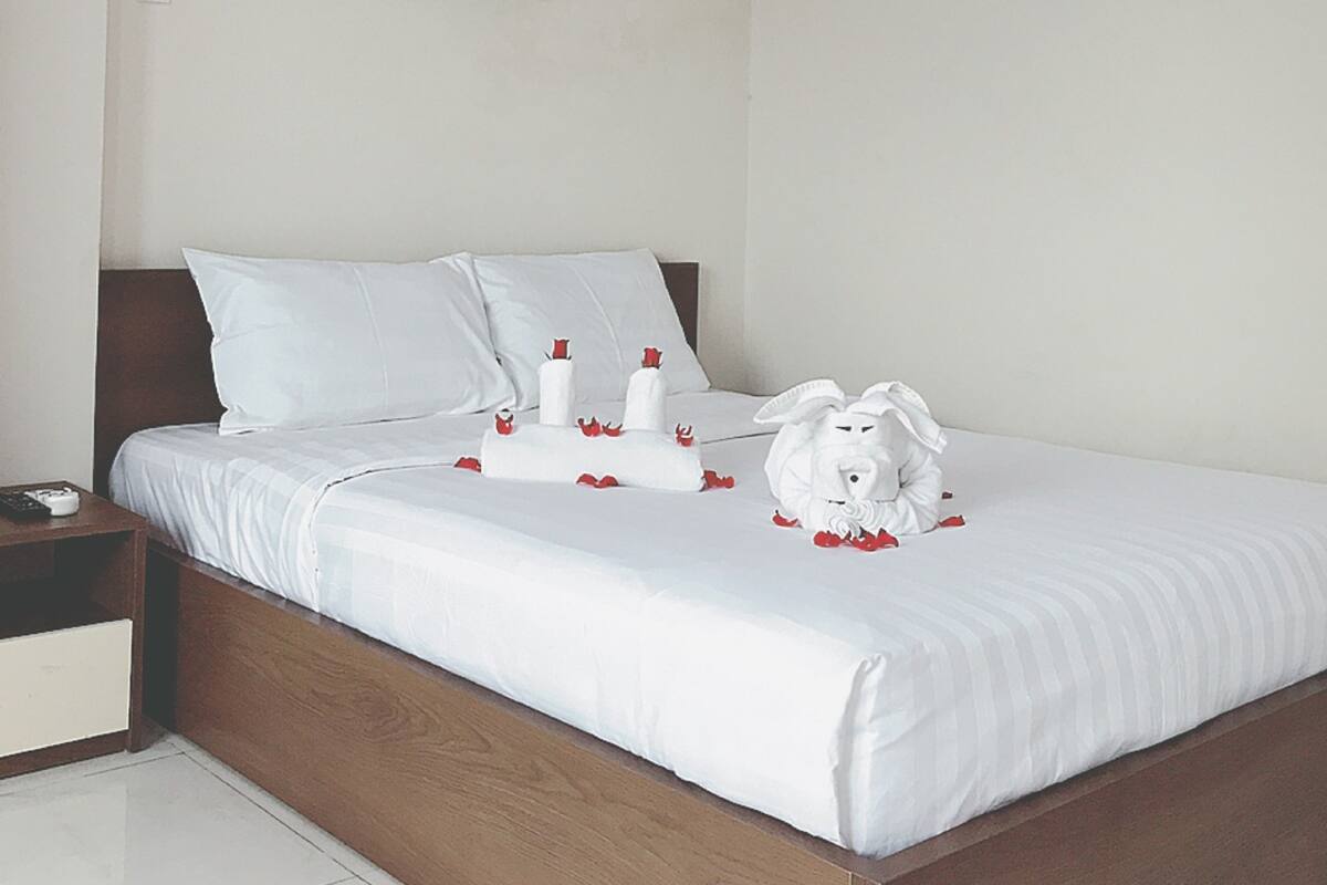 Una cama bien tendida con sábanas blancas, cabecera de madera y un cuadro en la pared.