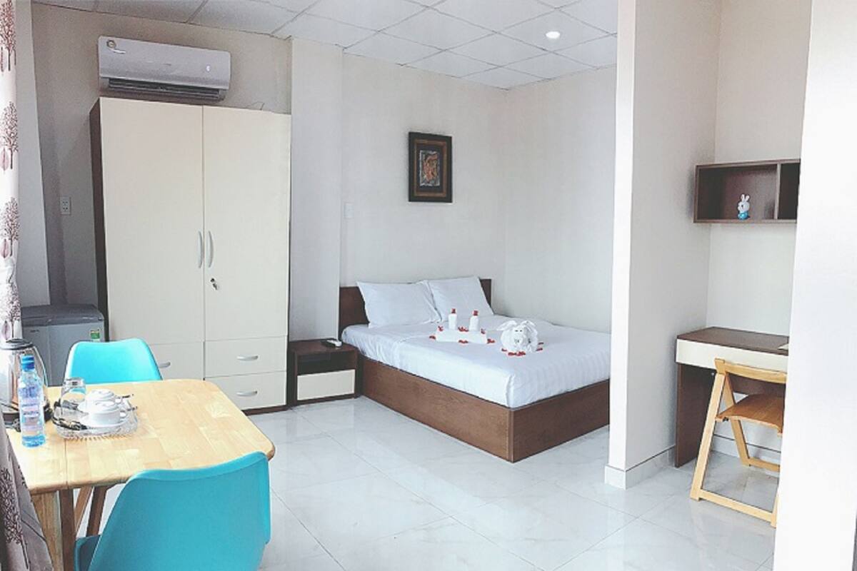Una habitación de hotel con cama, escritorio, silla, armario y aire acondicionado.