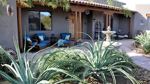 Una casa con un patio que cuenta con mobiliario exterior, una fuente decorativa y un jardín con plantas verdes grandes.