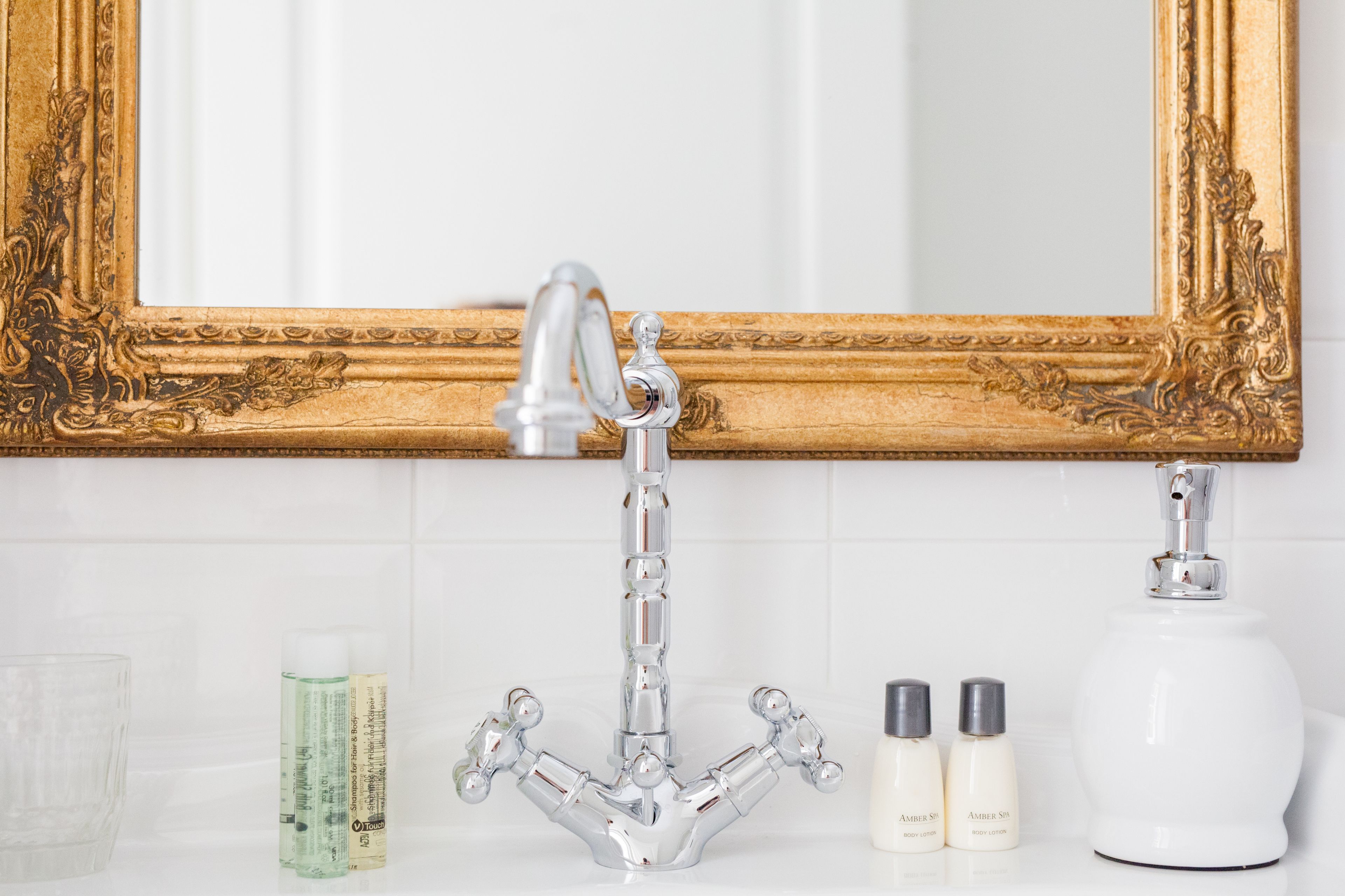 Une salle de bain avec un miroir à cadre doré, un robinet chromé et des articles de toilette posés sur le comptoir.