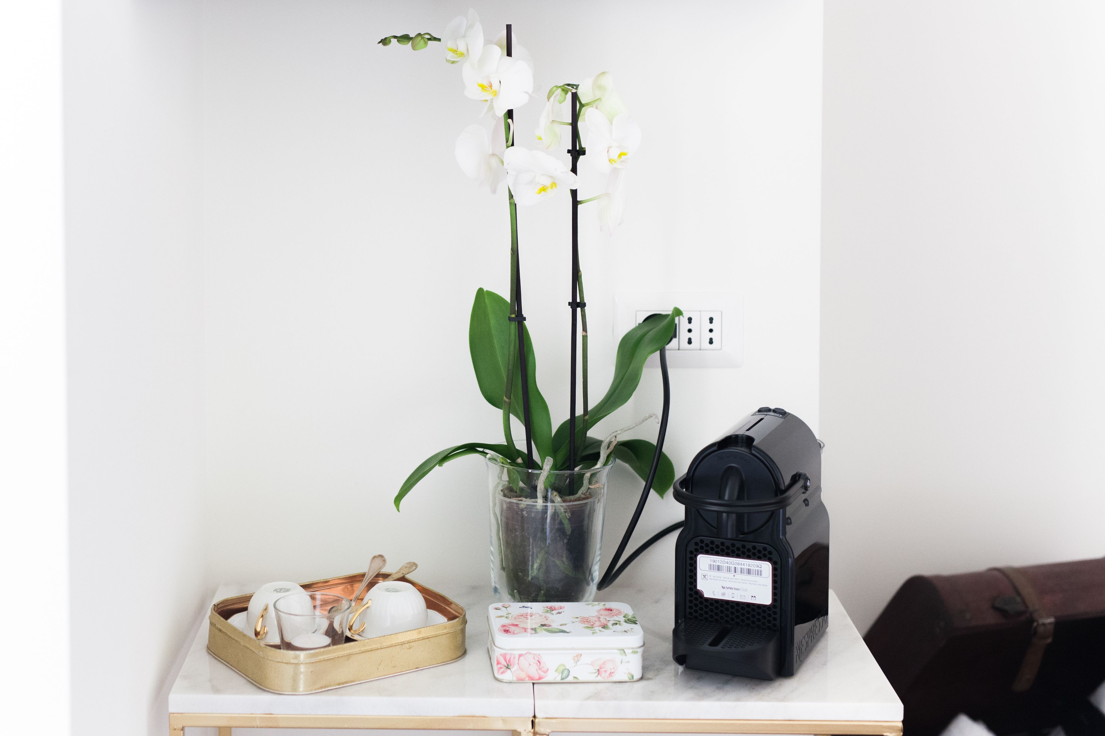 Un tavolo con un'orchidea in vaso, una macchina da caffè e un vassoio con tazze da tè e una teiera.