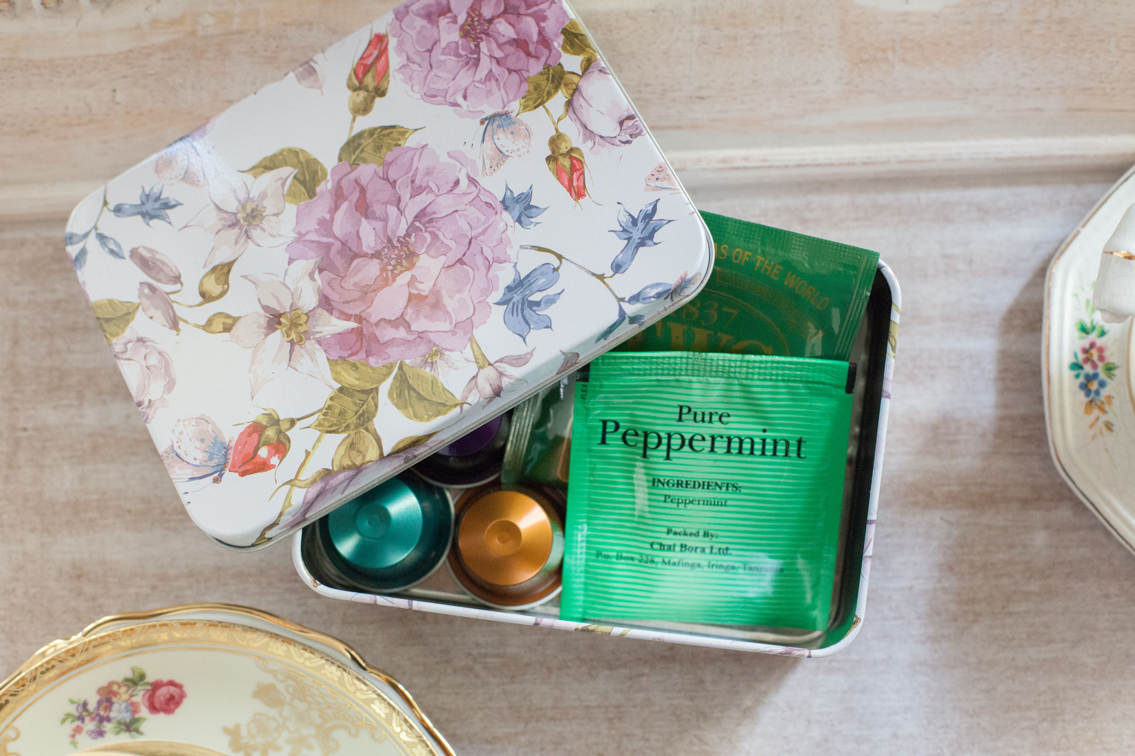 A floral-patterned tin box containing a green packet labeled "Pure Peppermint" and a few small containers.