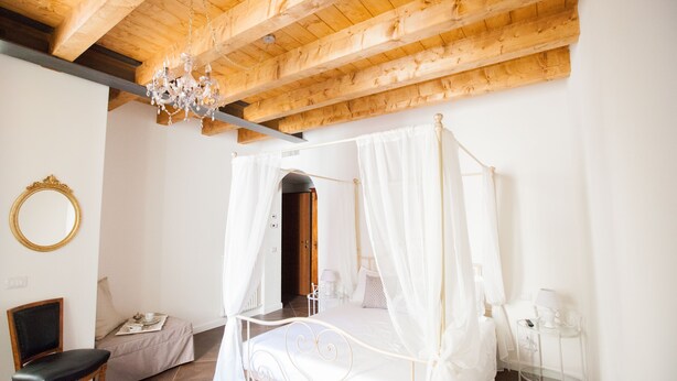 A bedroom with a four-poster bed, a wooden ceiling, a chandelier, a bedside table with a lamp, and a chair. - Alessia's Place (Como)
