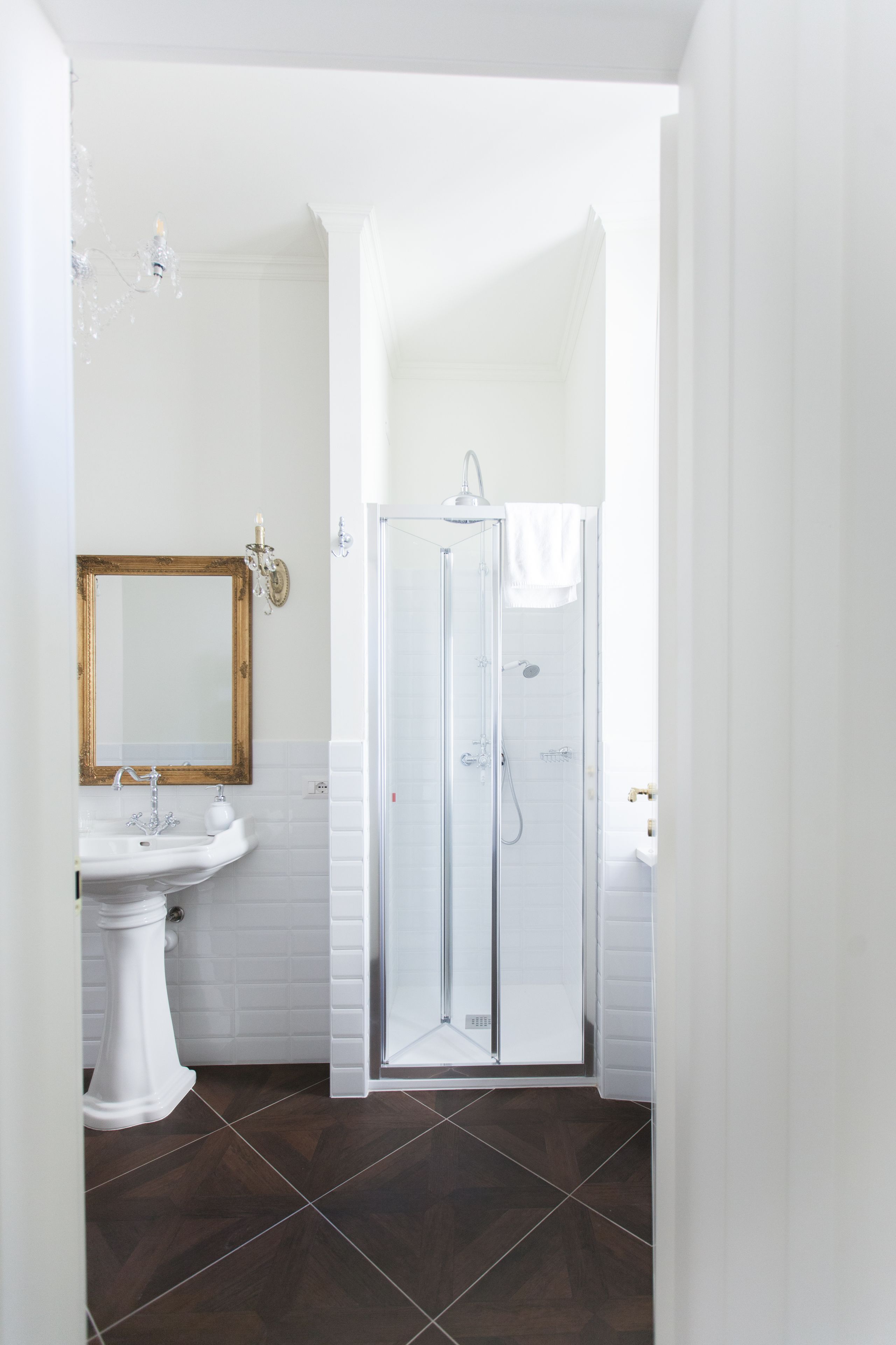 Ein Badezimmer mit einem weißen Waschbecken, einem Spiegel, einer Duschkabine und dunkelbraunen Fliesen.