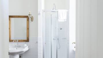 Ein Badezimmer mit einem weißen Waschbecken, einem Spiegel, einer Duschkabine und dunkelbraunen Fliesen.