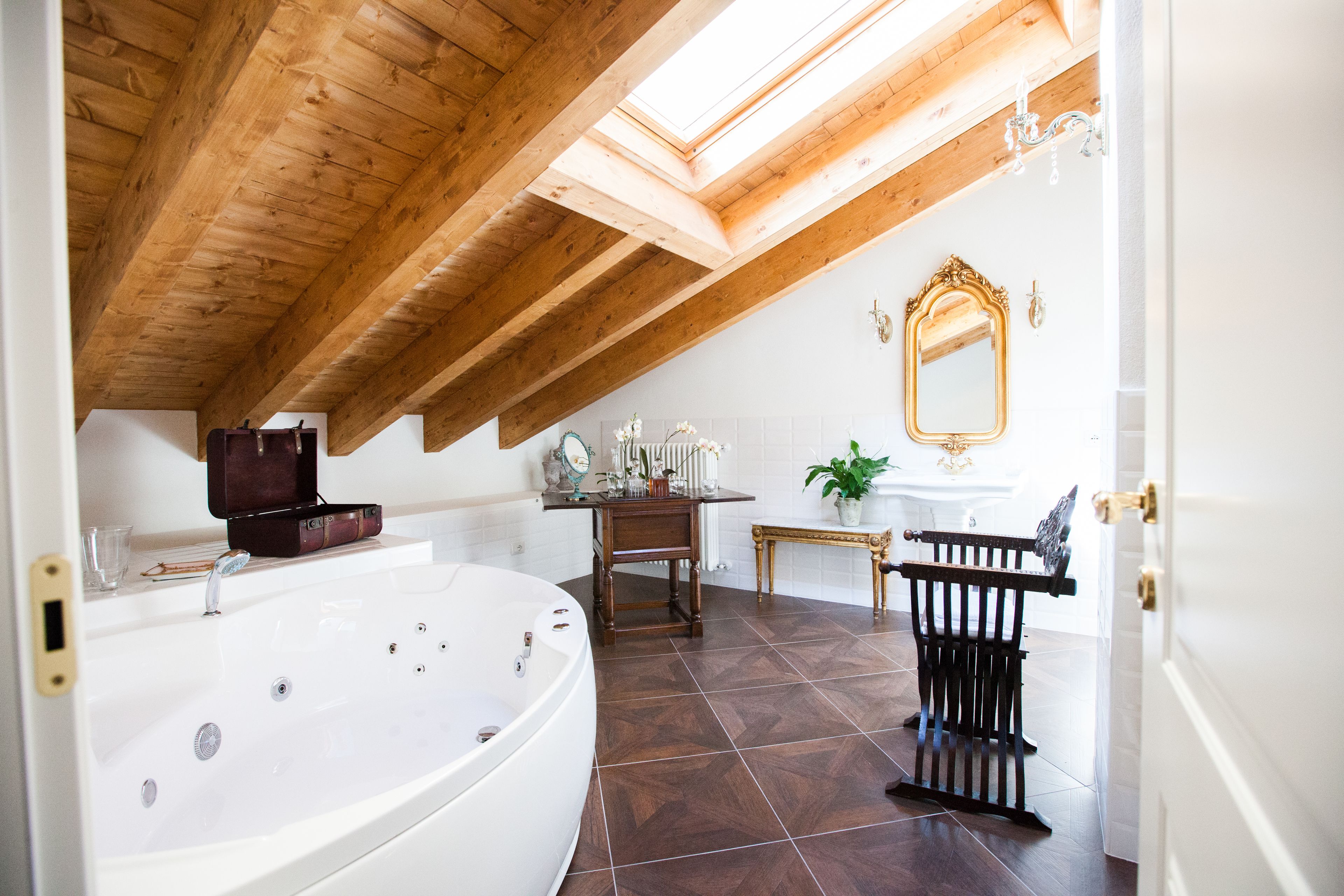 Un baño con una bañera independiente, vigas de madera en el techo, un tocador con espejo y una pequeña mesa con una planta.