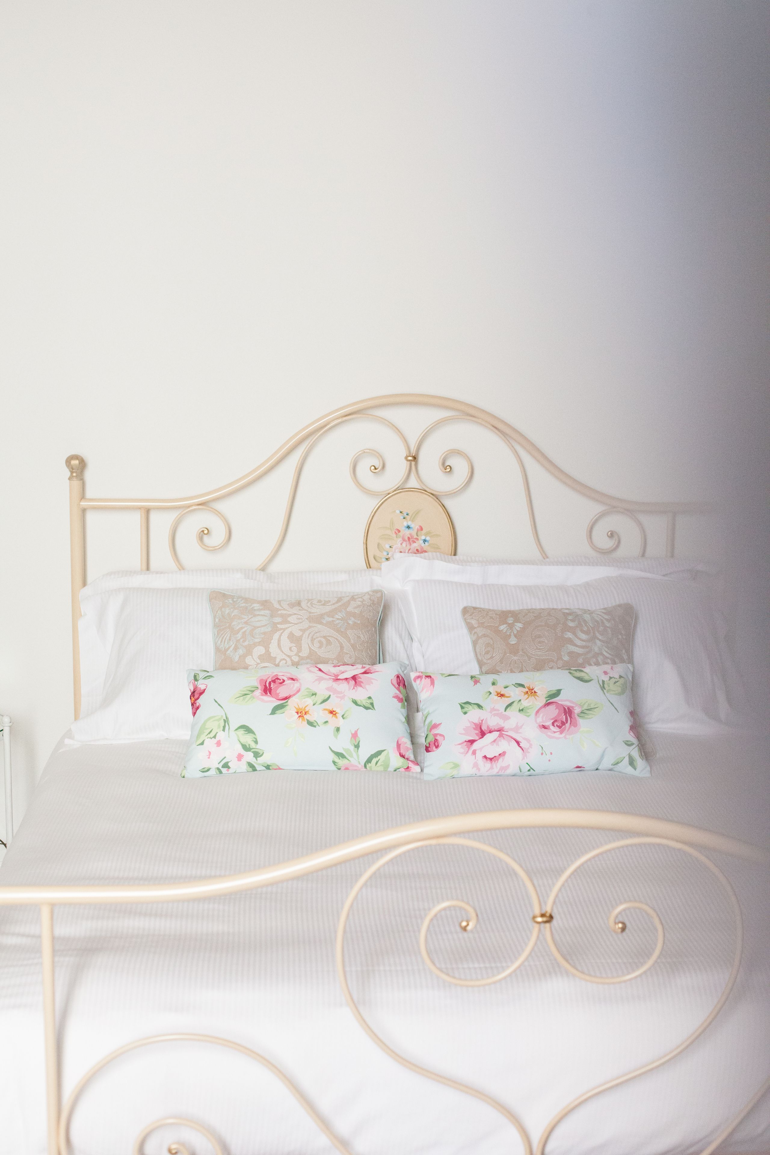 Ein Bett mit Metallgestell, weißer Bettwäsche und Kissen mit Blumenmuster.