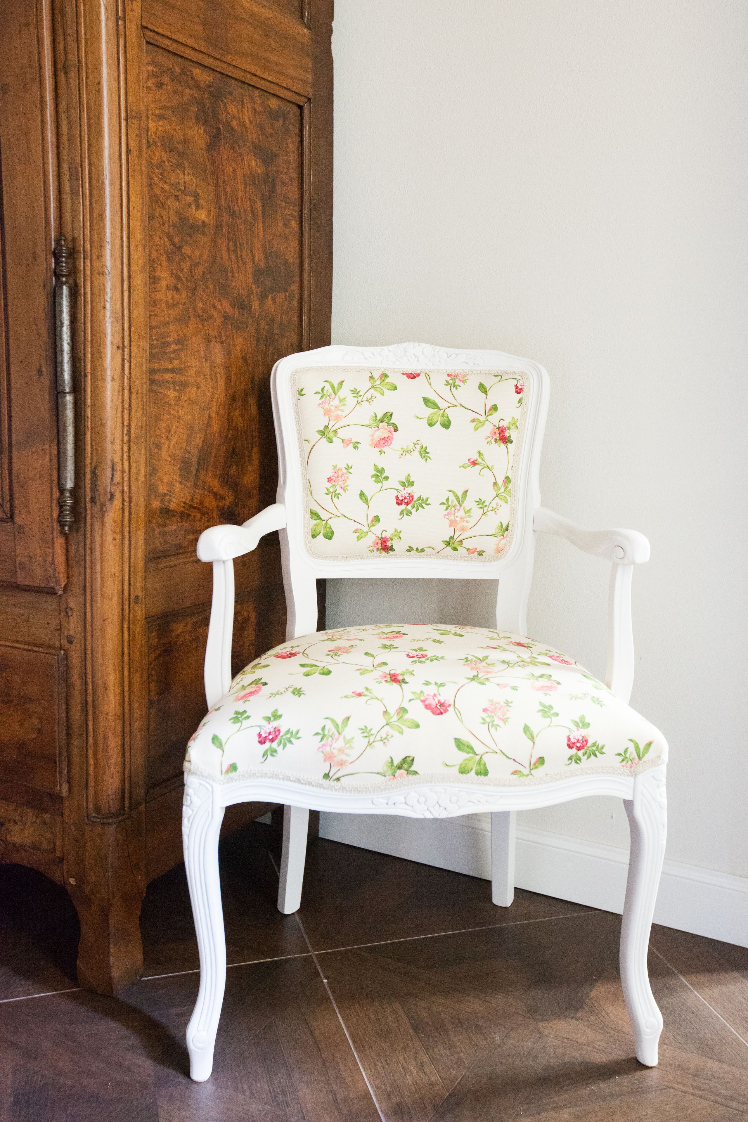 Una silla blanca con tapicería floral, ubicada frente a un aparador de madera.