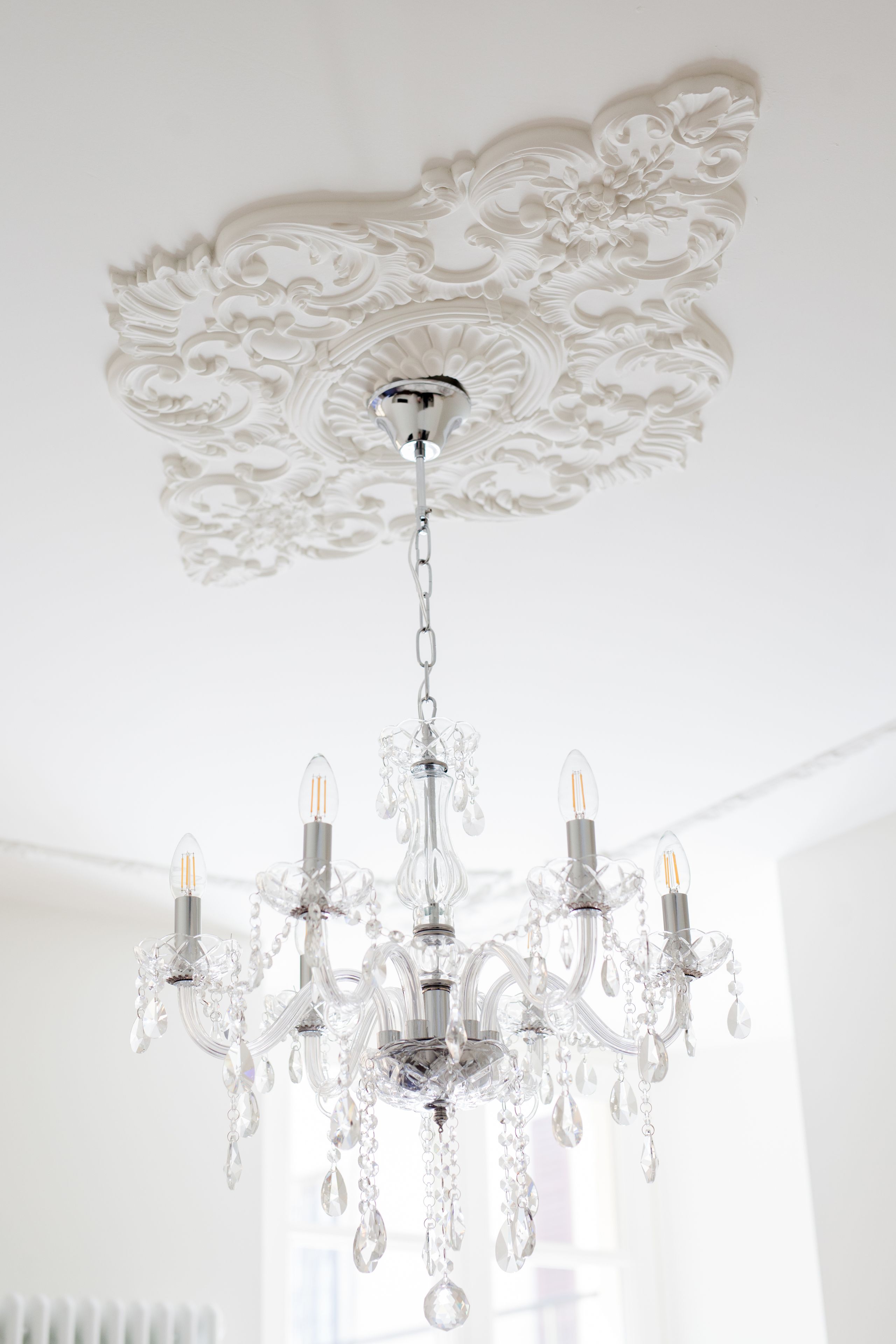 A chandelier with multiple arms and crystal details hanging from a ceiling with ornate plasterwork.