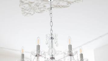 A chandelier with multiple arms and crystal details hanging from a ceiling with ornate plasterwork.