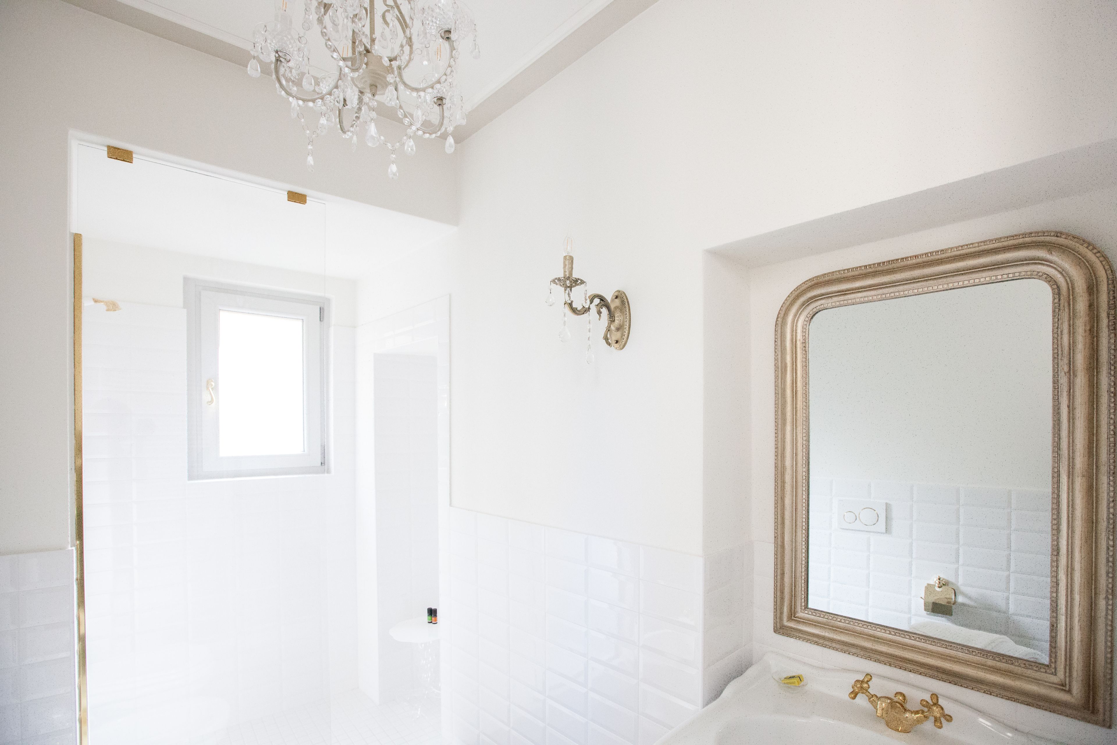 Un bagno con un grande specchio, piastrelle bianche e un lampadario.
