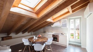 A dining area with a wooden table and chairs, a kitchen with white cabinets, and a skylight above. - Alessia's Place (Como)