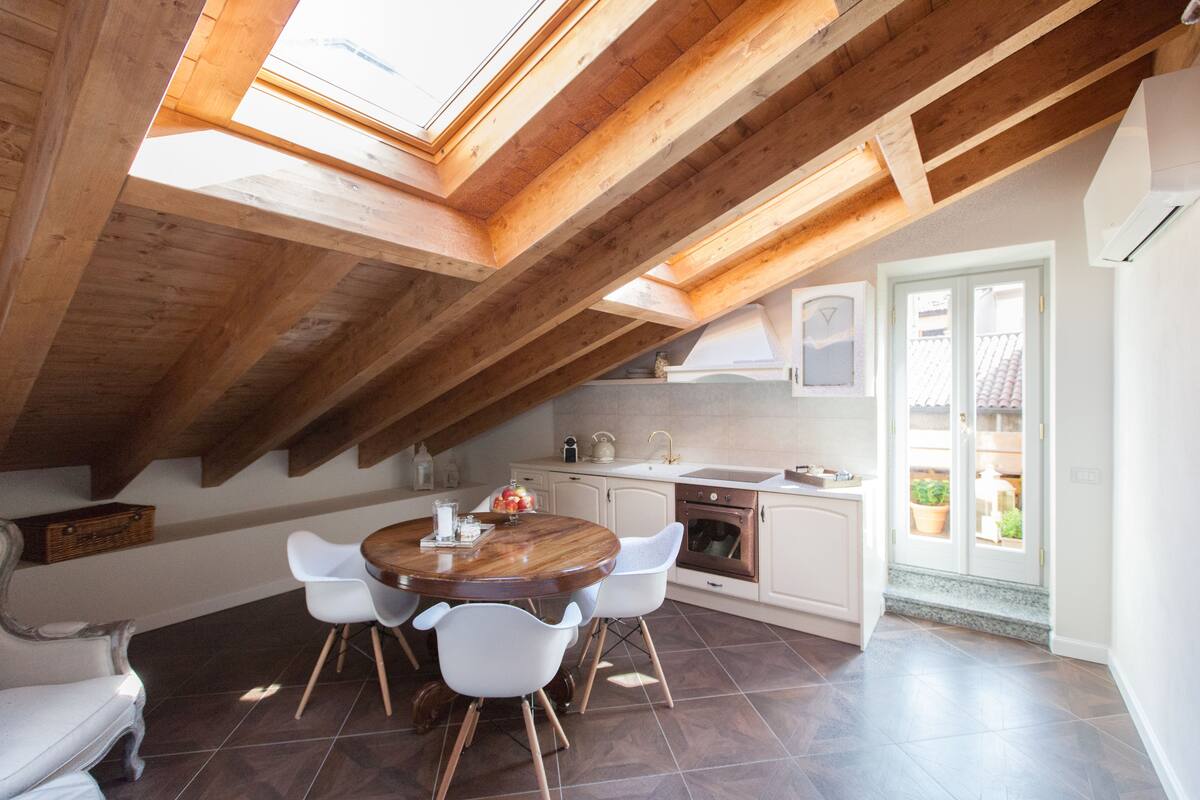 A dining area with a wooden table and chairs, a kitchen with white cabinets, and a skylight above.