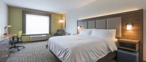Une chambre d’hôtel avec un grand lit, un bureau avec une chaise, une fenêtre et une lampe fixée au mur.