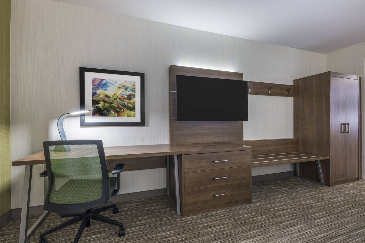 A hotel room with a wooden desk, a chair, a flat-screen TV, a cabinet, and a framed picture on the wall.
