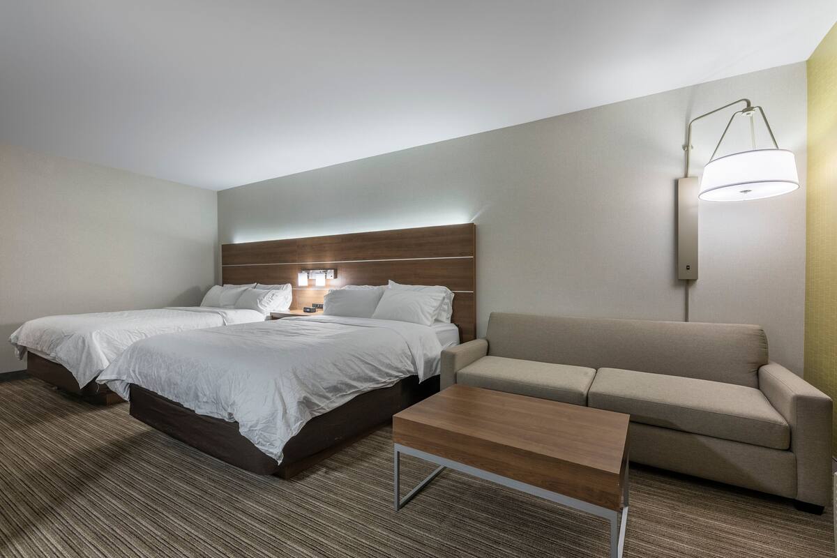 A hotel room with a large bed, a sofa, a wooden coffee table, and a wall-mounted lamp.