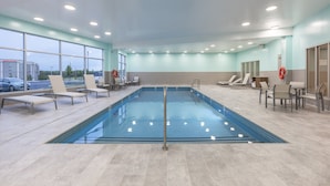 Una piscina interior amb parets de vidre transparent, diverses gandules i un sòl de rajoles.
