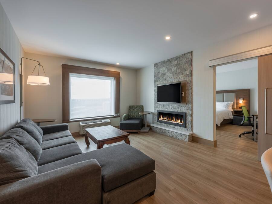 A modern living room with a sofa, a fireplace, a TV, and a large window.