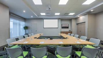 A conference room with a long table, chairs, a projector, and a screen.